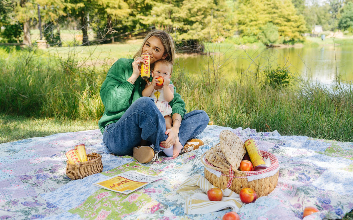 Sadie Robertson Huff on a picnic blanket with her daughter, sipping a 4GVN Half-Caff